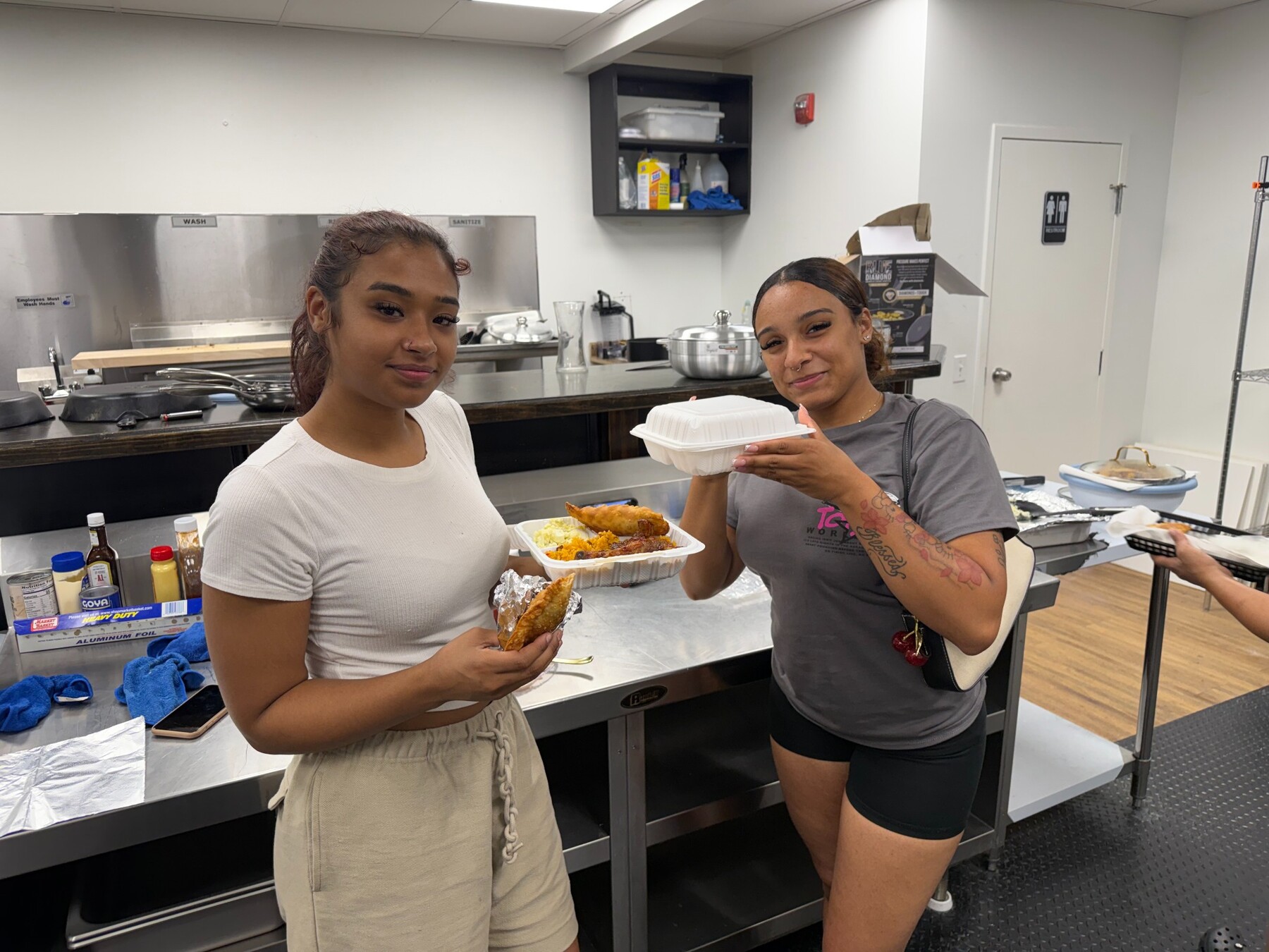 Two guests holding freshly prepared Acruz meals in the kitchen